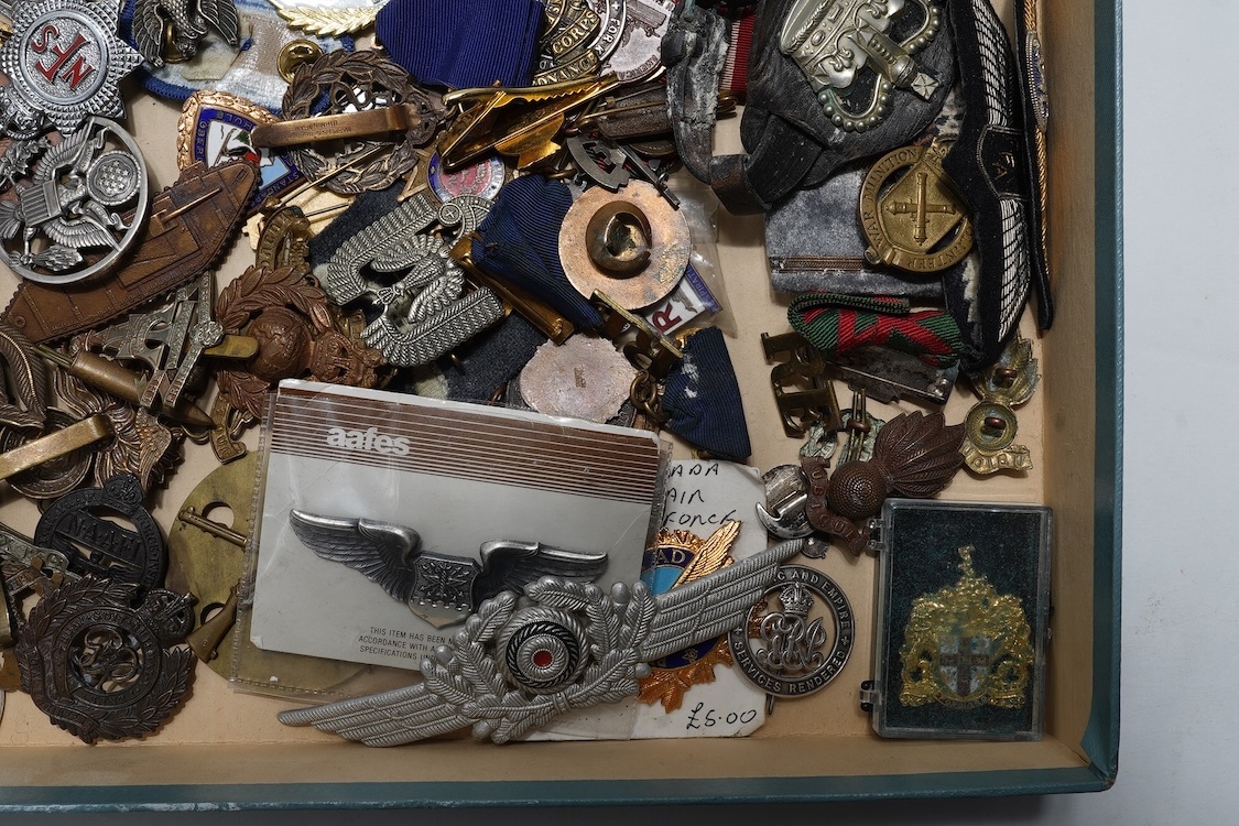 A collection of primarily 20th century military badges, lapel badges, shoulder titles, and other related ephemera, including seventeen military cap badges, cloth badges, ARP badges, etc., together with a military tin box